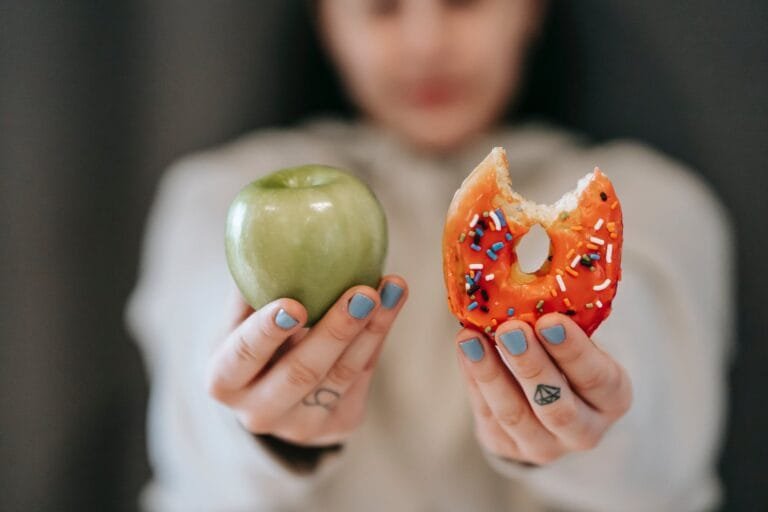 Cambio de hábitos para sentirte más ágil 1 woman showing apple and bitten doughnut