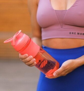 crop faceless sportswoman standing with reusable water bottle